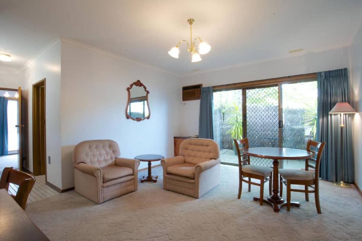A living room with two armchairs, a sofa, a round table with chairs, a chandelier, and a large window with curtains.