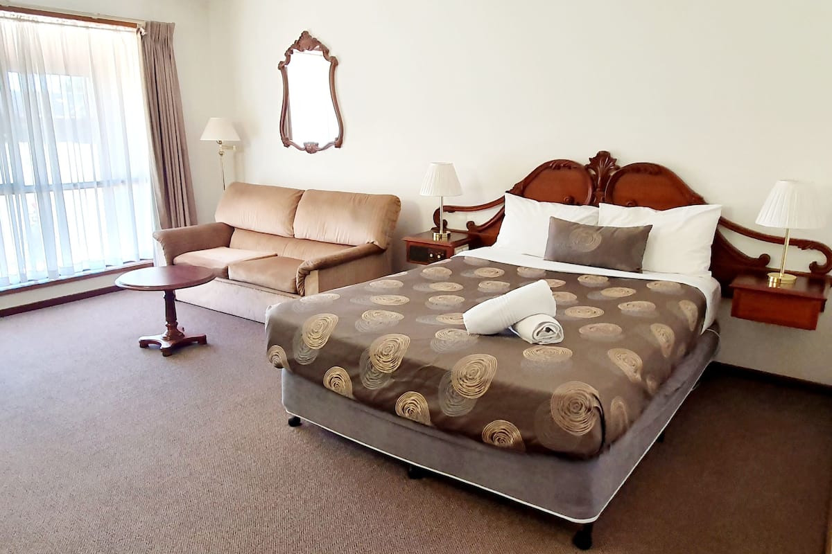 A hotel room with a large bed, a sofa, a small table, and a nightstand with lamps.