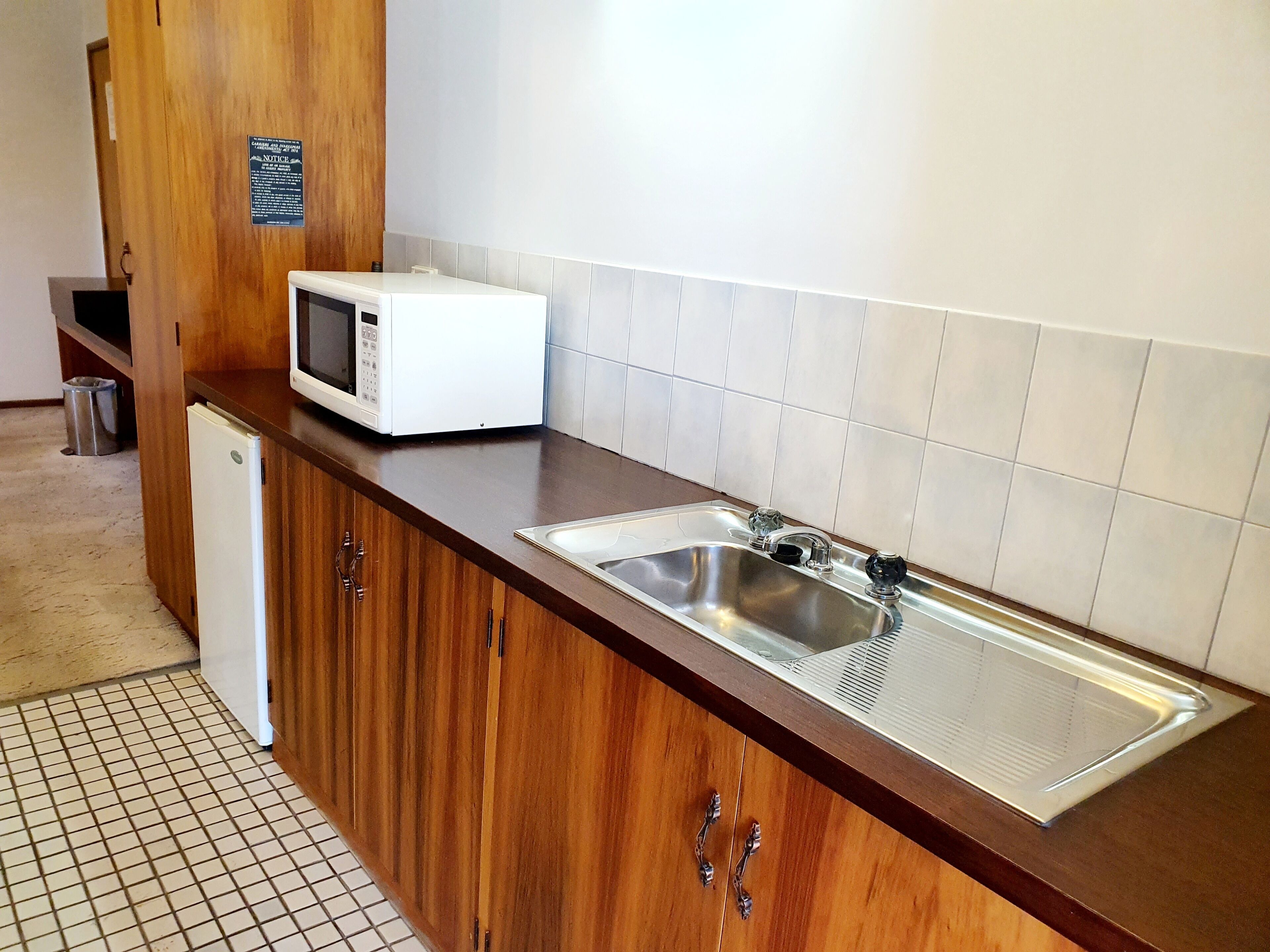 Una cocina con un lavamanos de acero inoxidable, un microondas y armarios de madera.