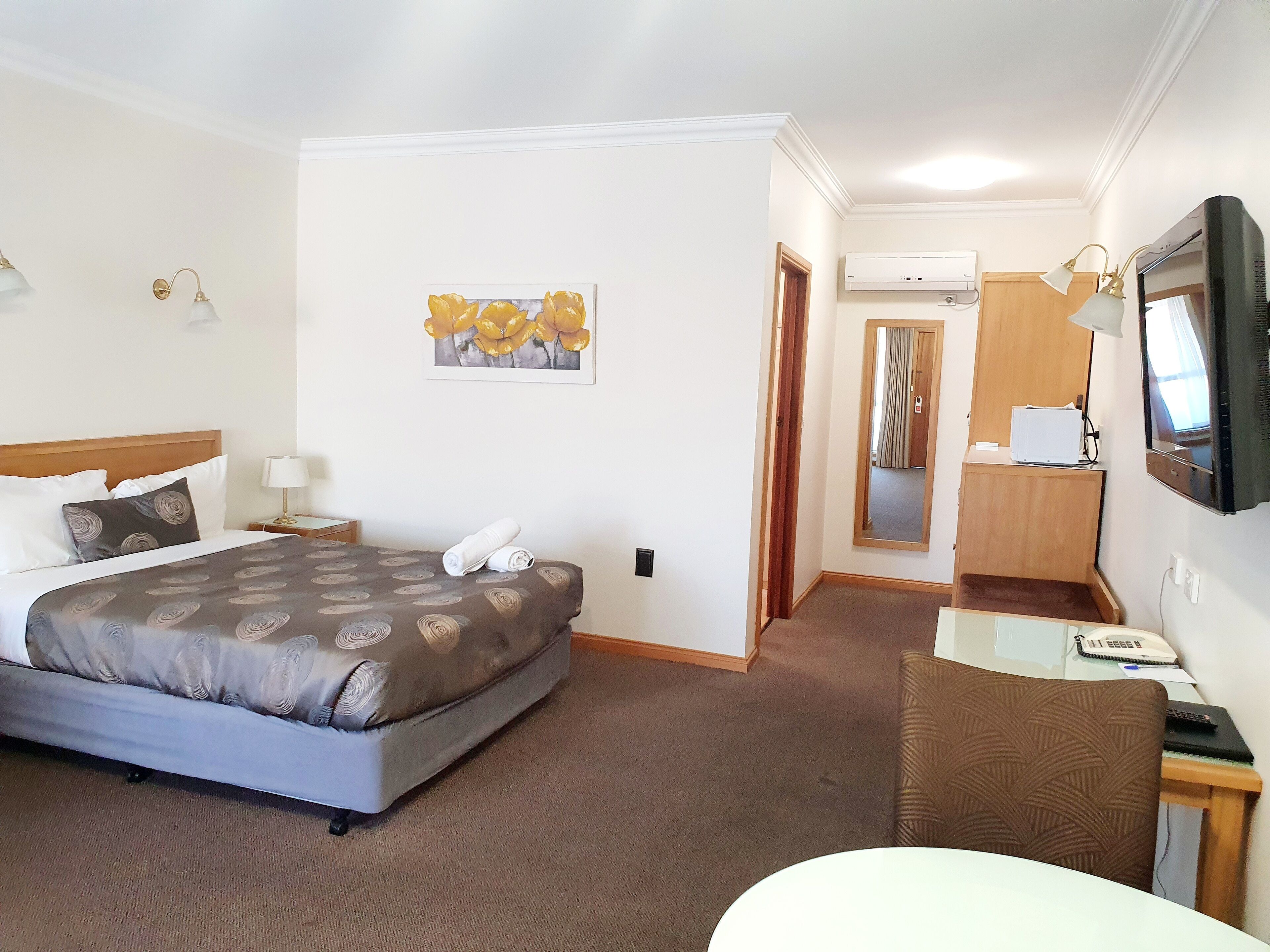 Quarto de hotel com cama, secretária, cadeira, televisão e ar condicionado.