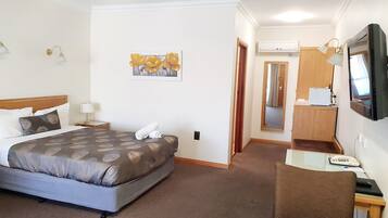 Quarto de hotel com cama, secretária, cadeira, televisão e ar condicionado.