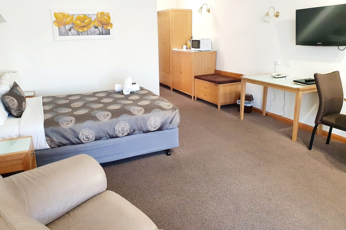 A hotel room with a bed, a desk, a chair, a television, and a wardrobe.