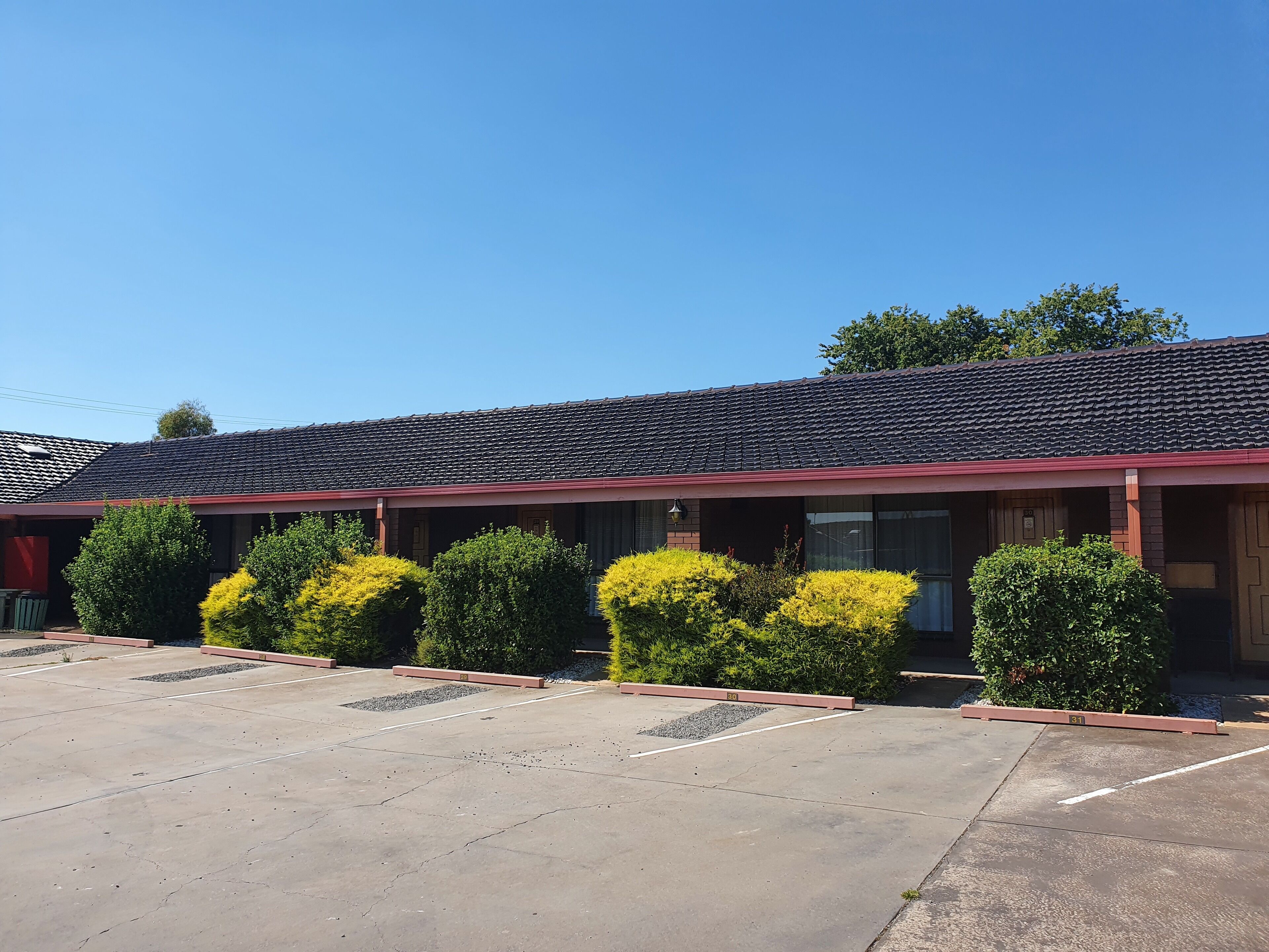 A motel with a tiled roof, a parking lot, and neatly trimmed bushes.