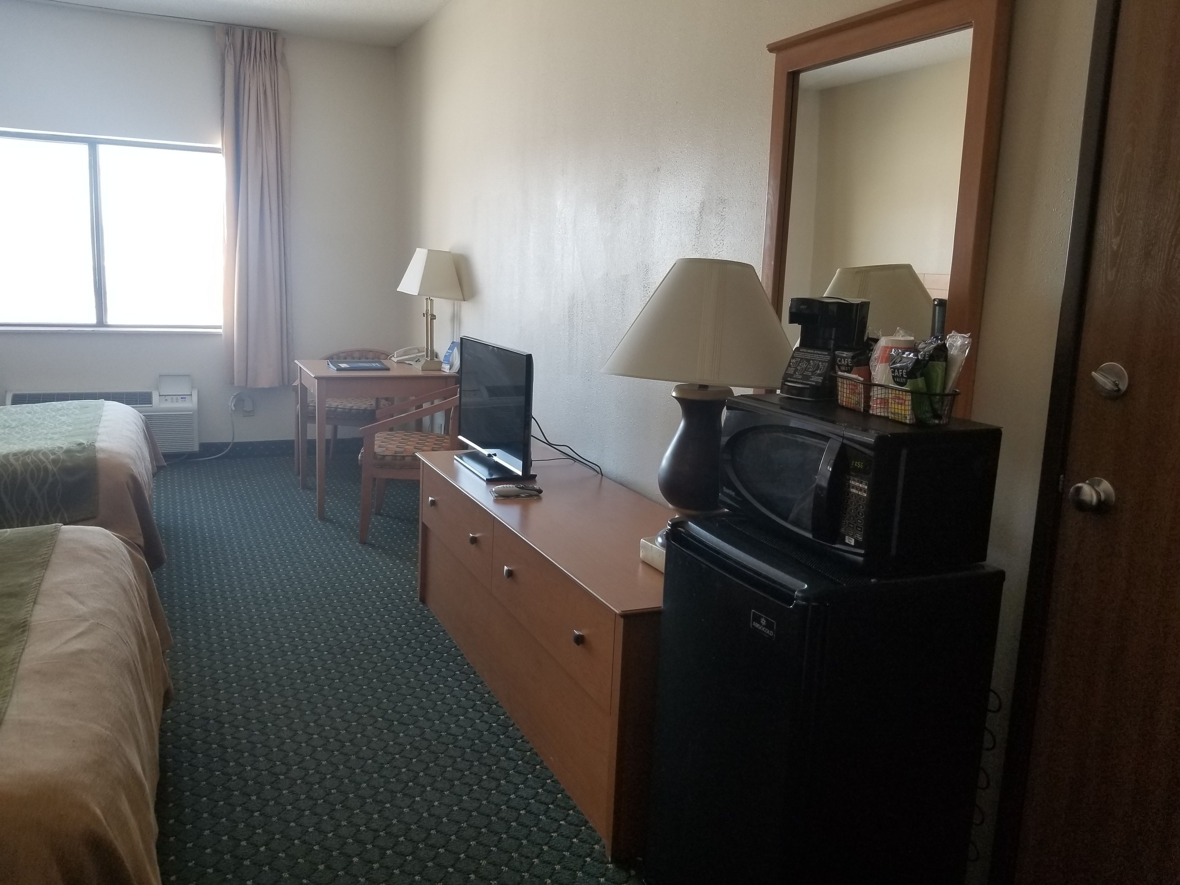 Una camera d'albergo con due letti, una scrivania con un computer, una televisione, una macchina del caffè e un frigorifero.