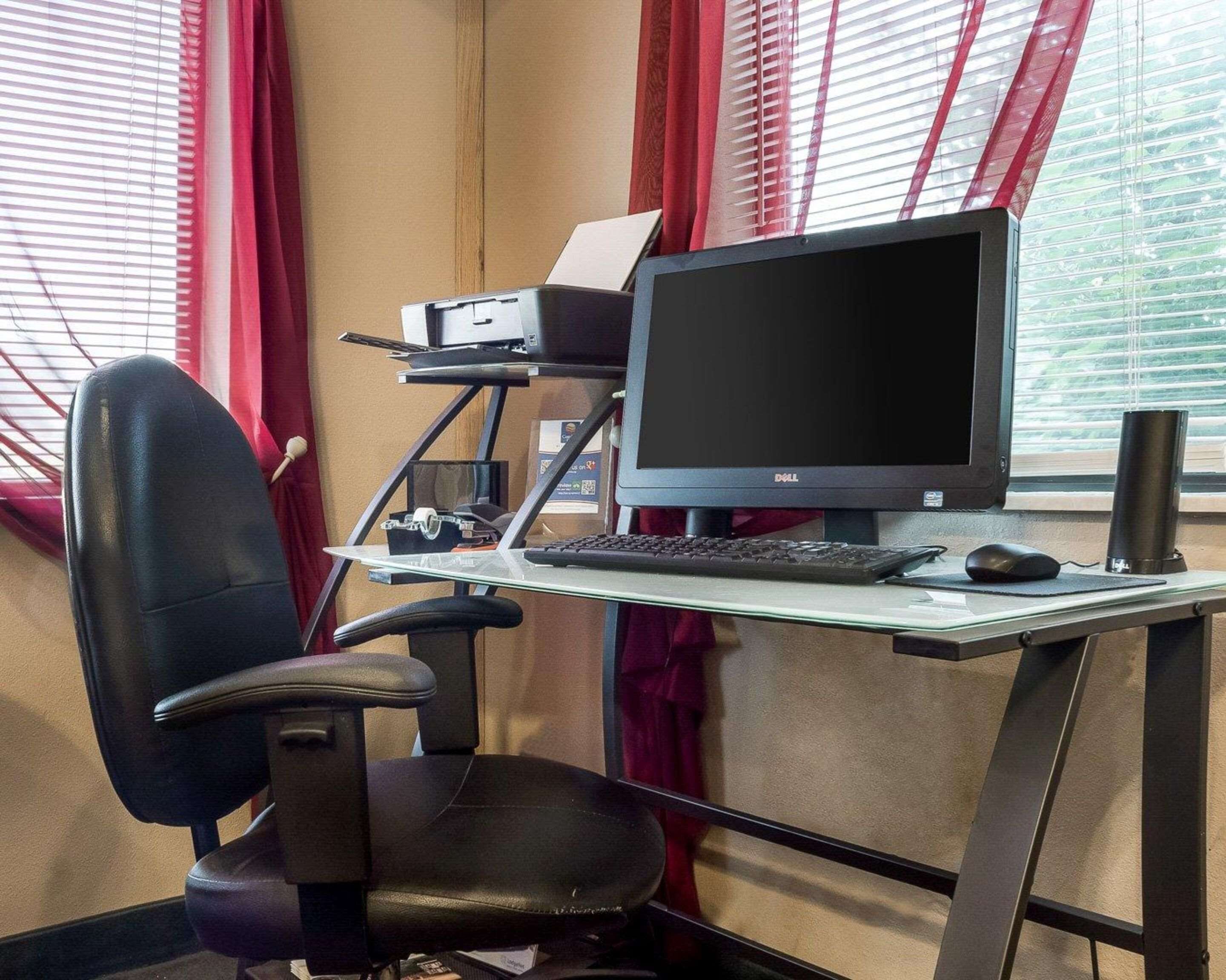 A home office setup with a Dell monitor, keyboard, and mouse on a glass desk, a black office chair, and a printer.