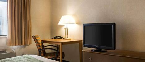Een hotelkamer met een bed, een bureau met lamp, een televisie en een stoel.