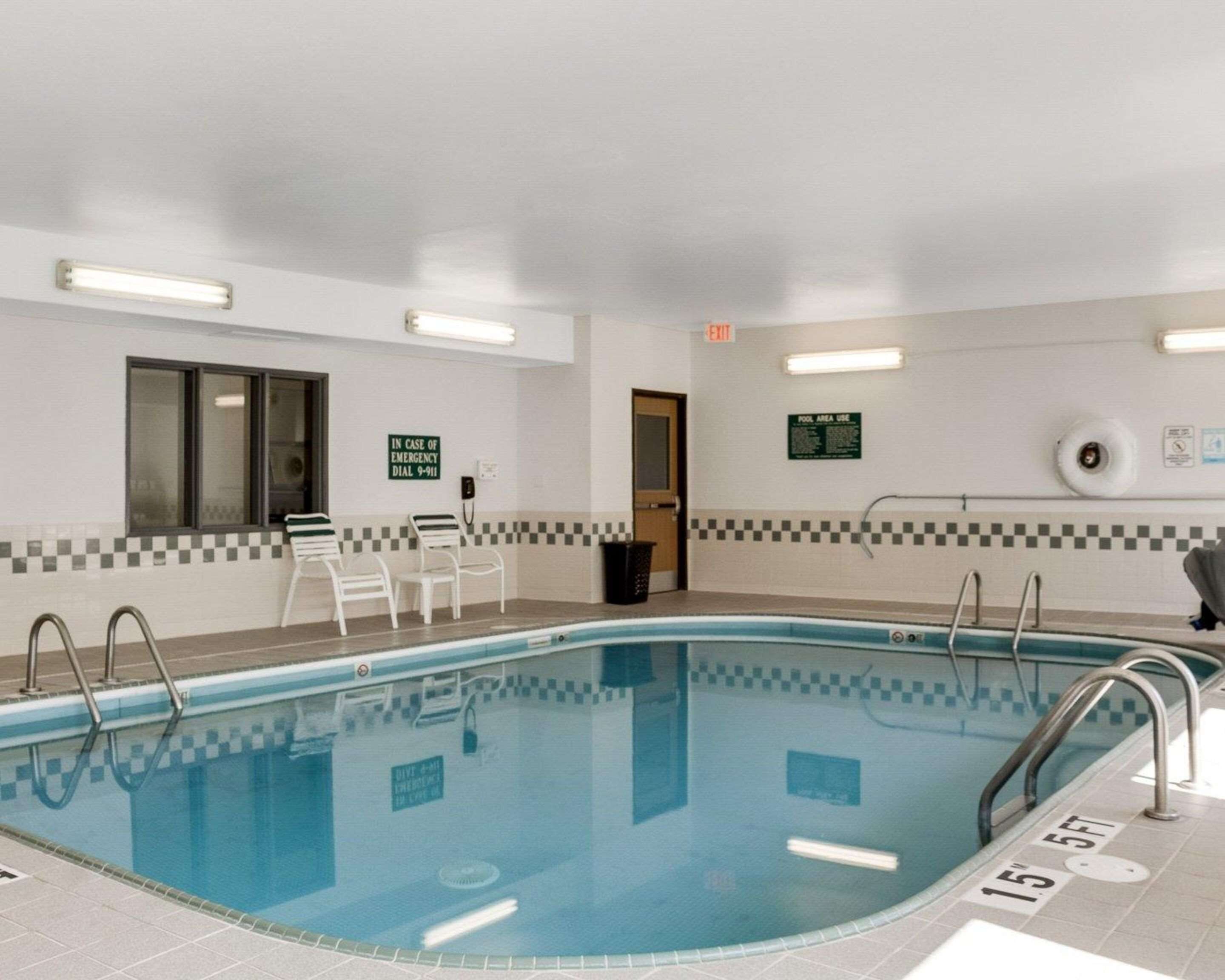 Uma piscina com borda de azulejos xadrez, uma cadeira de salva-vidas e uma placa com o número de emergência 9-1-1.