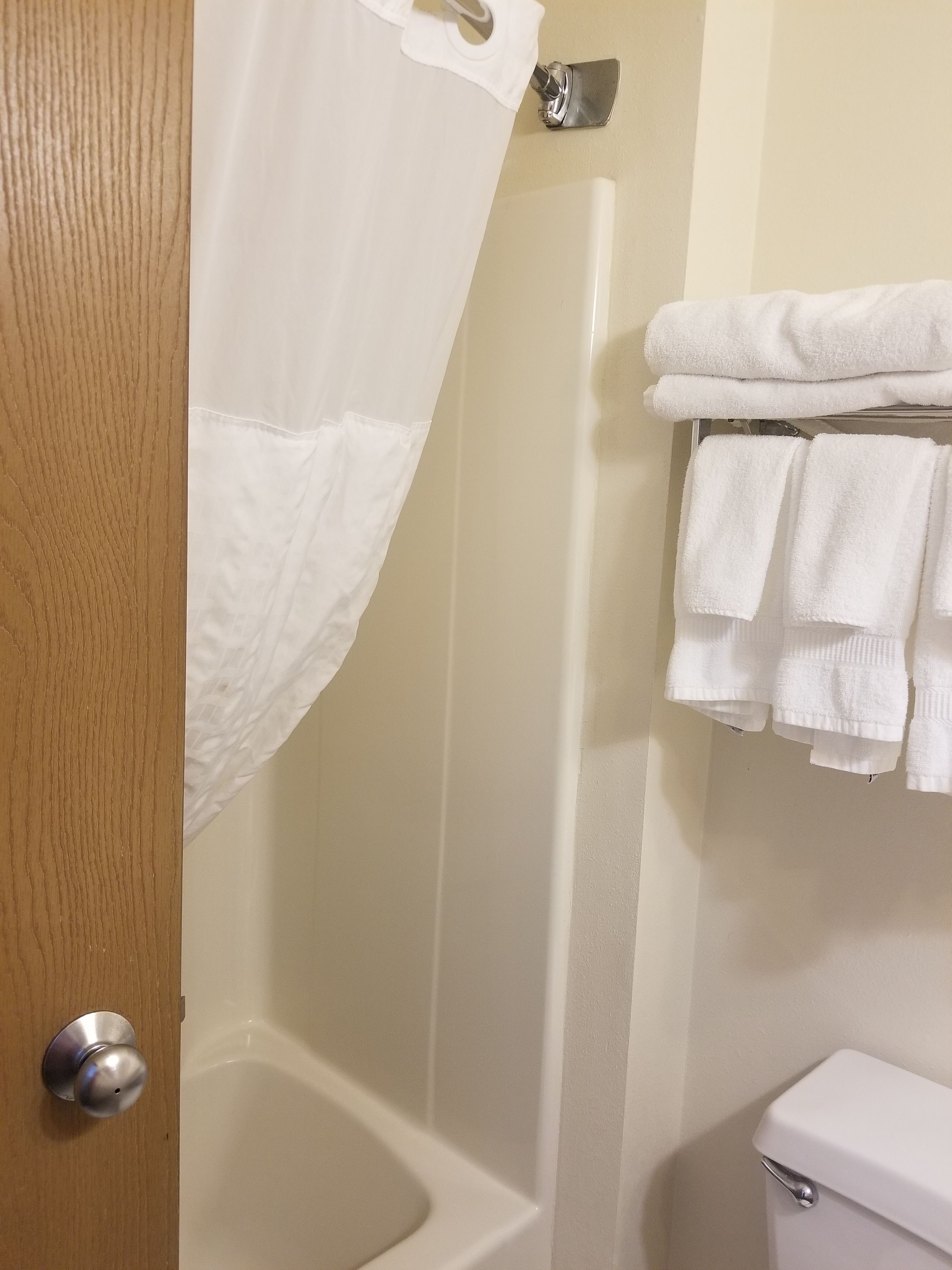 A bathroom with a shower curtain, a bathtub, and a stack of white towels on a rack.