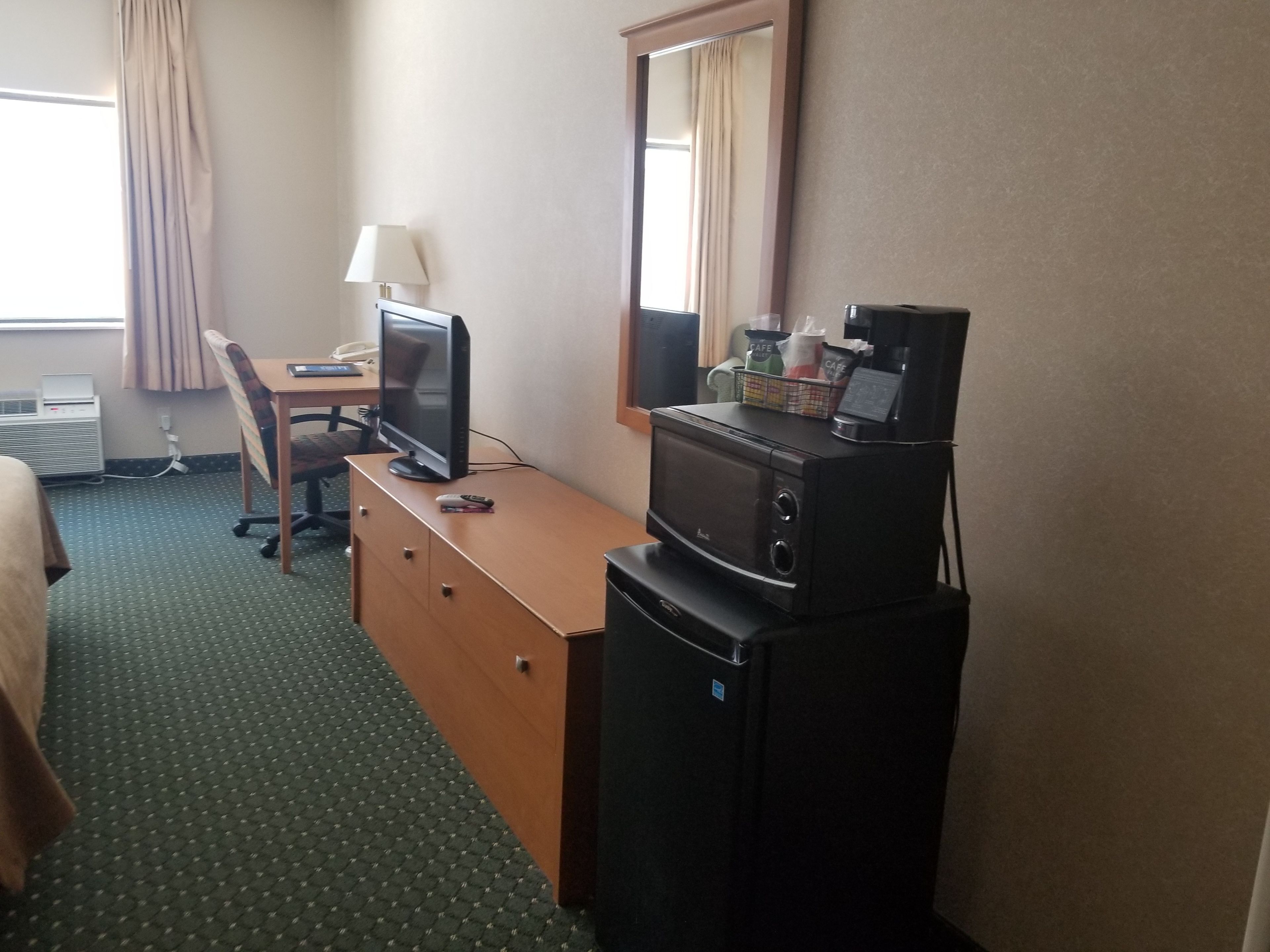 A hotel room with a bed, a desk with a computer, a television, a refrigerator, and a microwave.