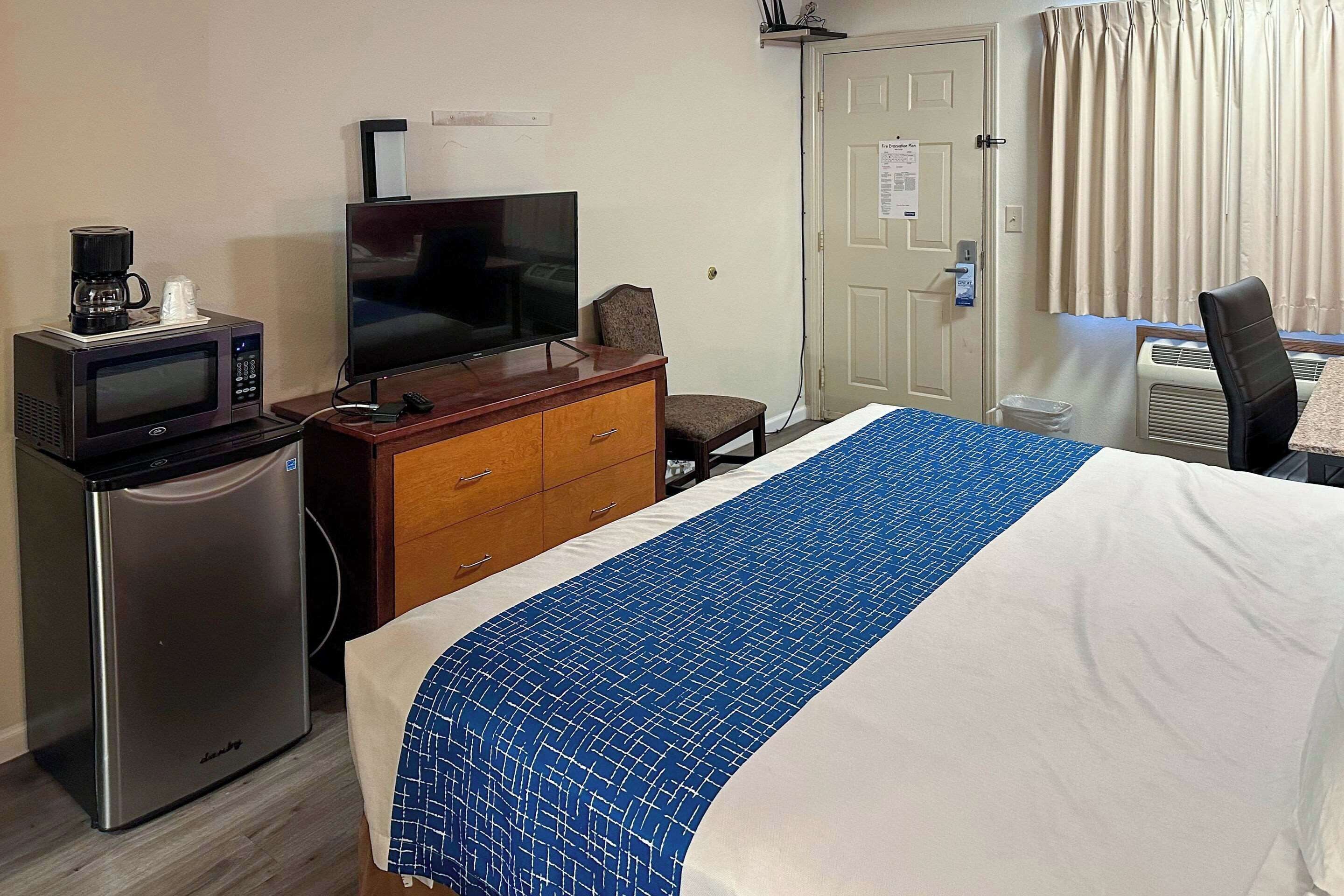 A hotel room with a bed, a desk, a television, a microwave, and a refrigerator.