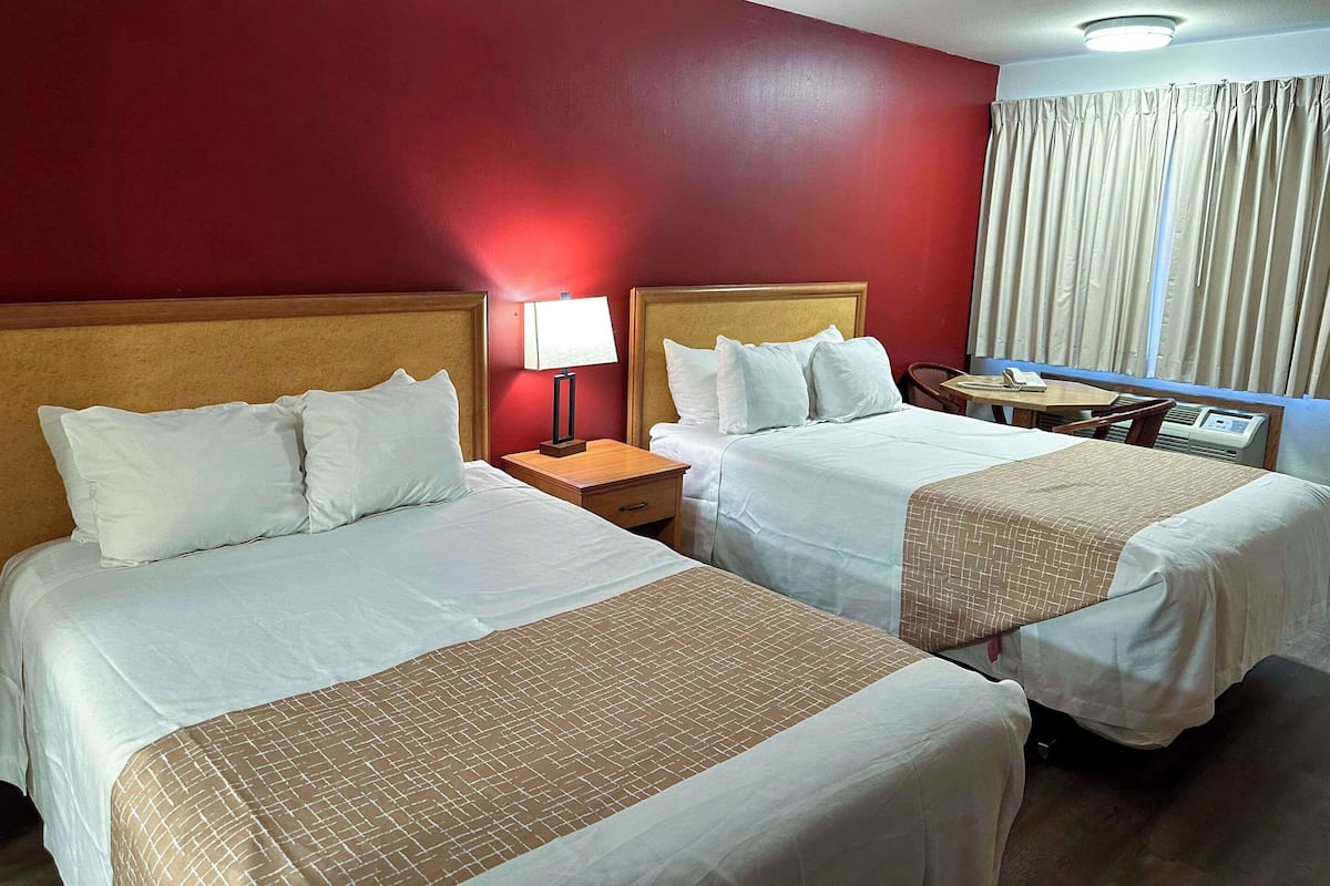 Habitación de hotel con dos camas, una mesita de noche con lámpara, una pequeña mesa con teléfono y una ventana con cortinas.