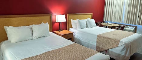 A hotel room with two beds, a nightstand with a lamp, a small table with a phone, and a window with curtains.