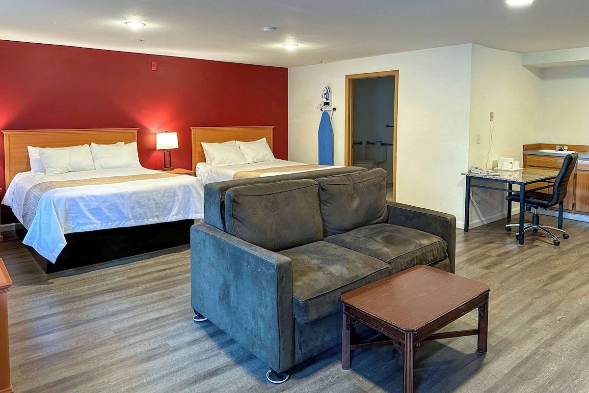 Una habitación de hotel con dos camas, un sofá, una mesita, un escritorio y una silla.