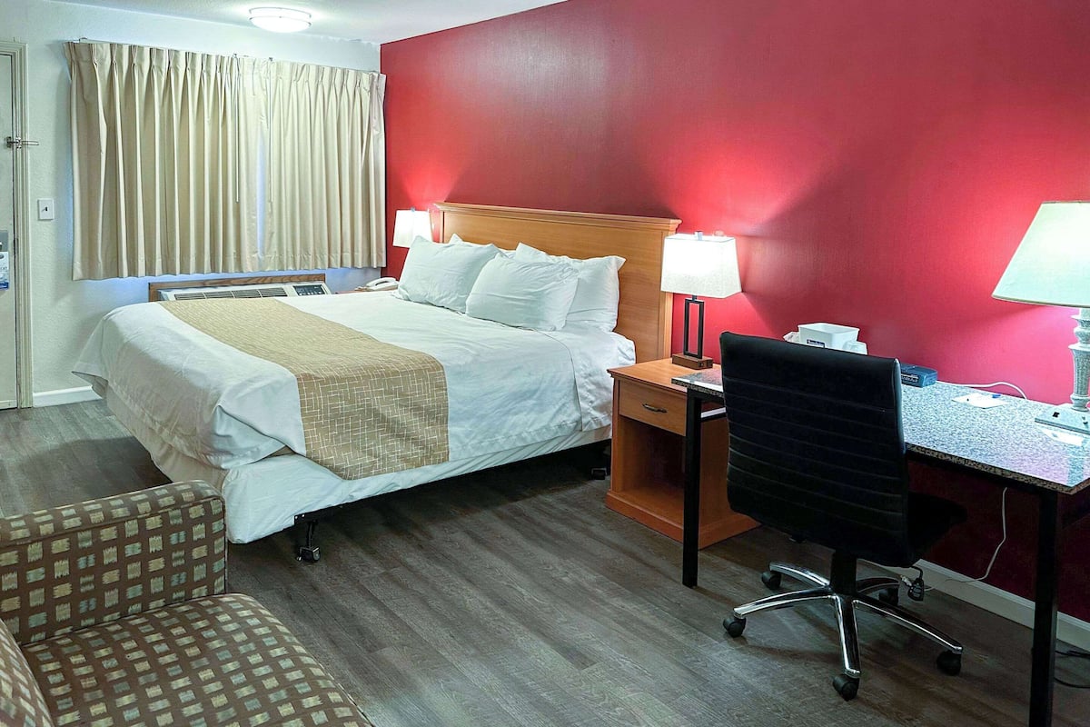 Habitación de hotel con cama, escritorio, silla y pared roja.
