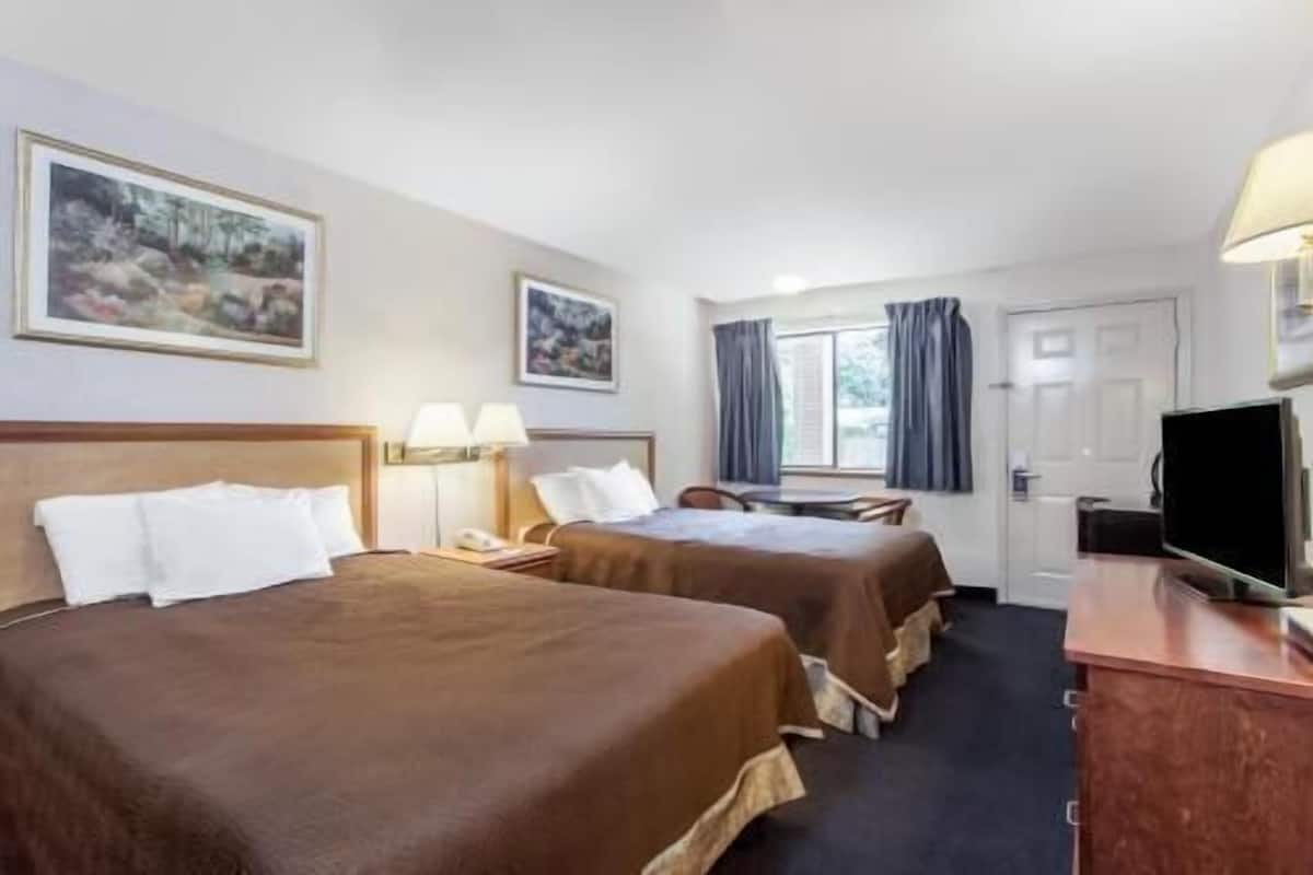 Habitación de hotel con dos camas, un escritorio, un televisor y una ventana con cortinas.