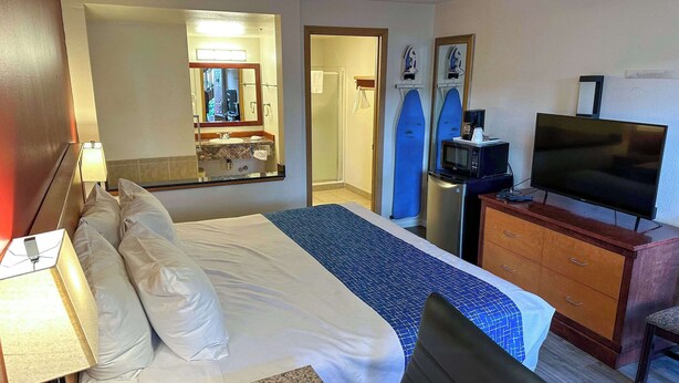 A hotel room with a bed, a desk with a television, a mirror, a shower, and a surfboard. - Econo Lodge Edmonds North Seattle (Edmonds)