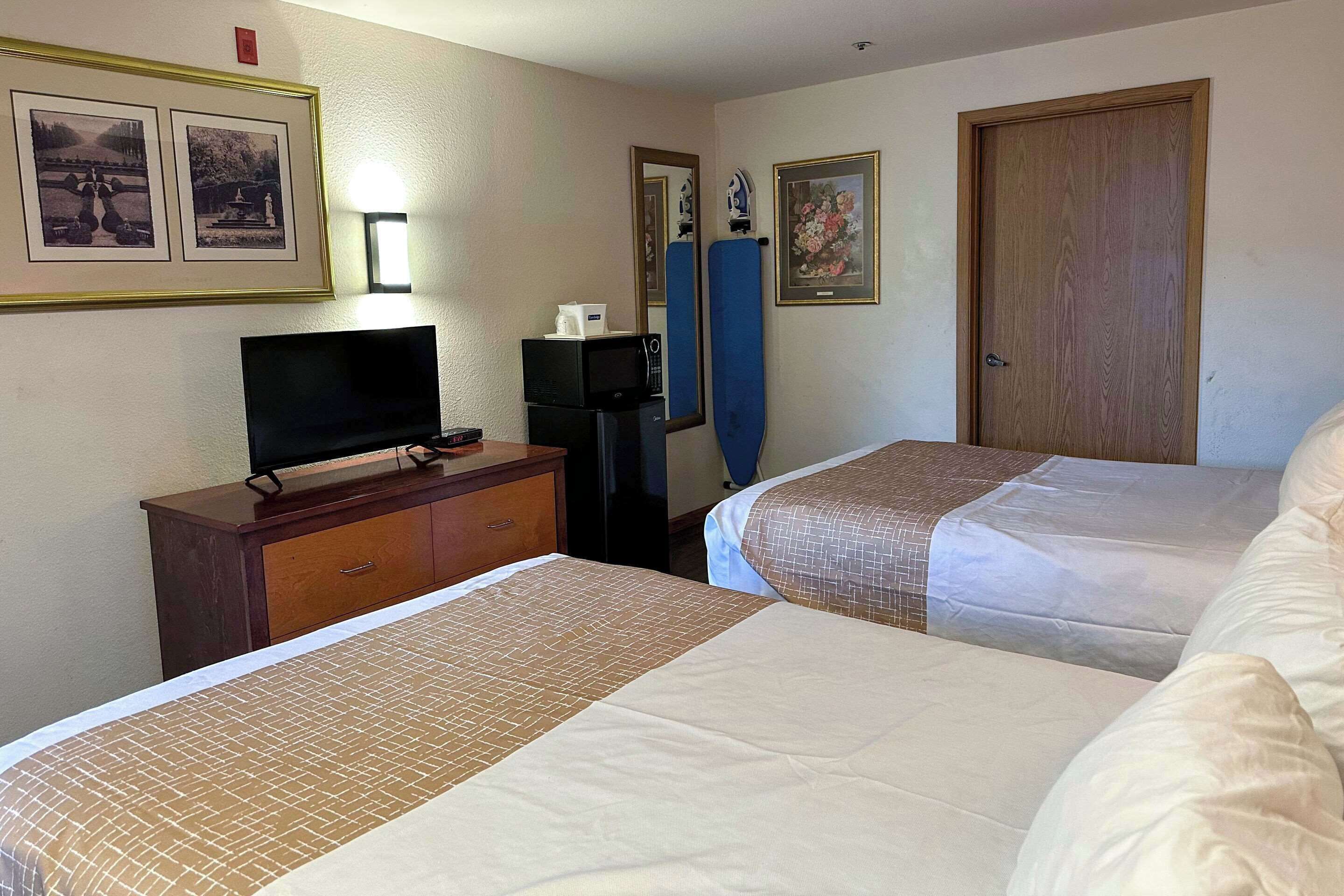 A hotel room with two beds, a TV on a dresser, and framed pictures on the wall.
