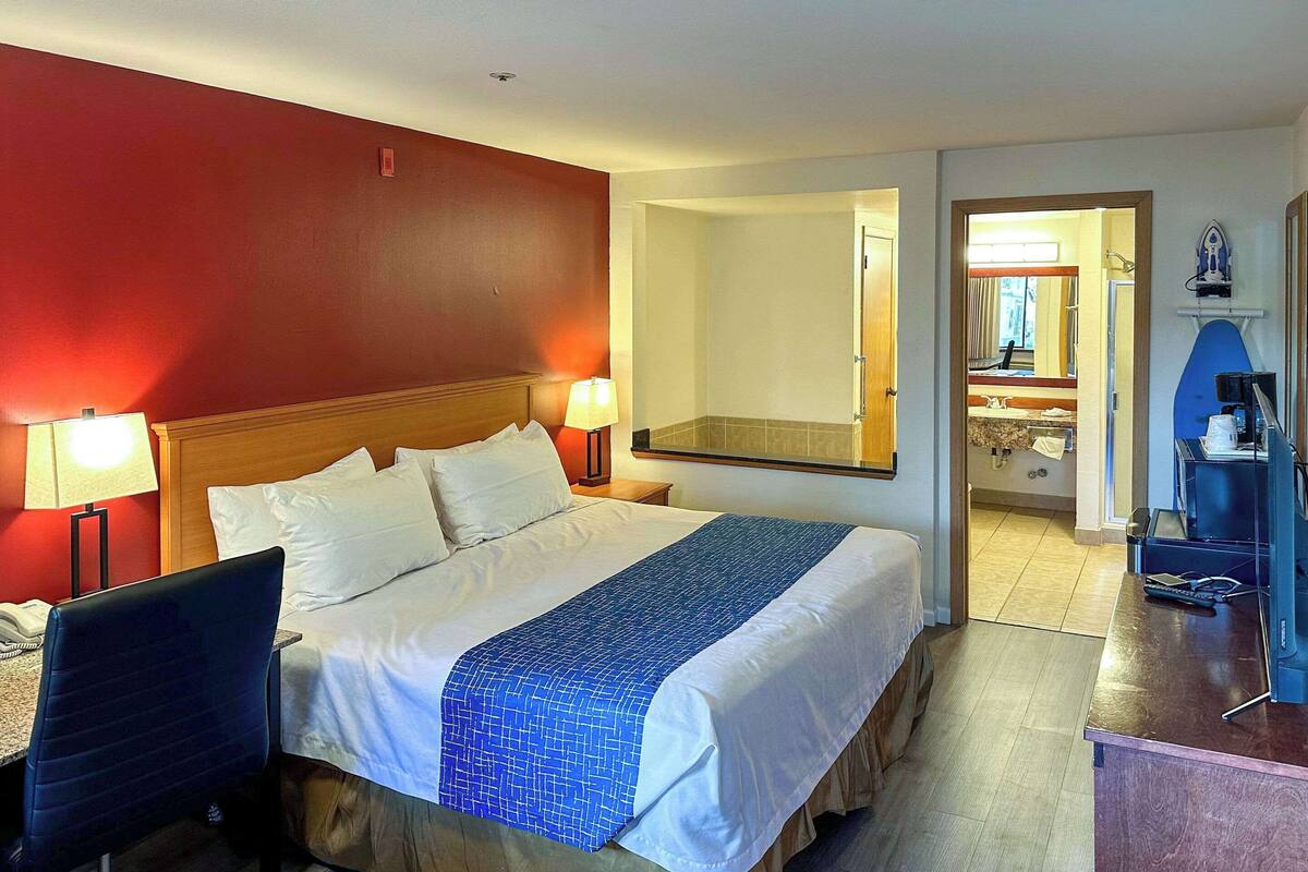 Habitación de hotel con cama, lámparas de noche, un escritorio con computadora y un espejo.