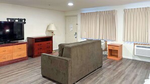 A living room with a sofa, a TV, a lamp, a small table, and a window with curtains. - Econo Lodge Edmonds North Seattle (Edmonds)