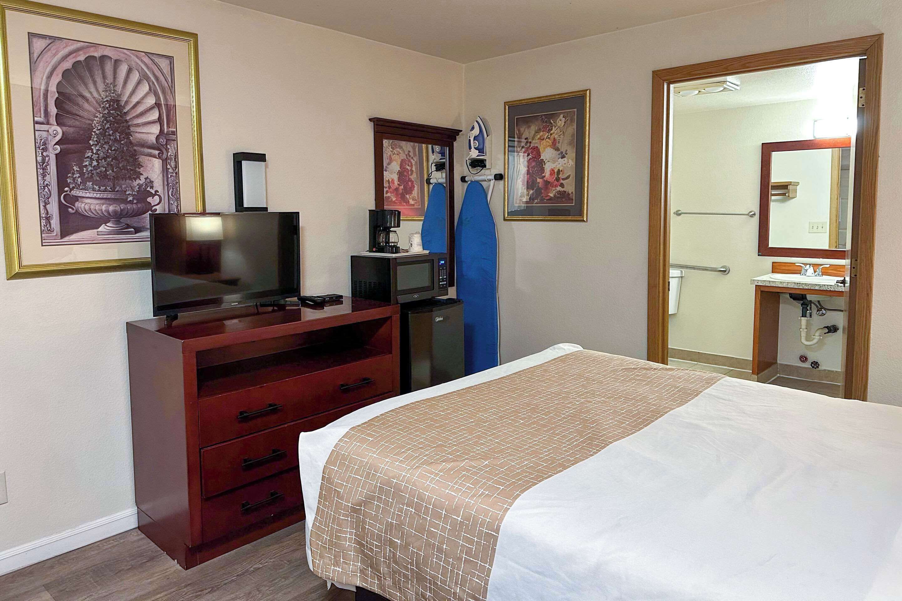 A hotel room with a bed, a TV, a microwave, a dresser, and a bathroom visible through an open door.
