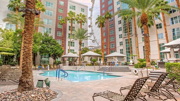 A hotel pool area with palm trees, lounge chairs, and a Ferris wheel in the background. - Hilton Grand Vacations Club Flamingo Las Vegas (Las Vegas)