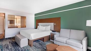 Une chambre d’hôtel avec un grand lit, un canapé, une table de chevet et un miroir avec des stores verticaux.