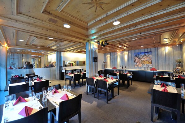 A restaurant with wooden ceiling beams, tables set with red napkins, and a large mural on the wall. - Hotel Sommerau (Chur)