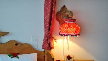 A wooden bed with a white pillow and a red rose. A small wooden table with a glass vase and a red rose is next to the bed.