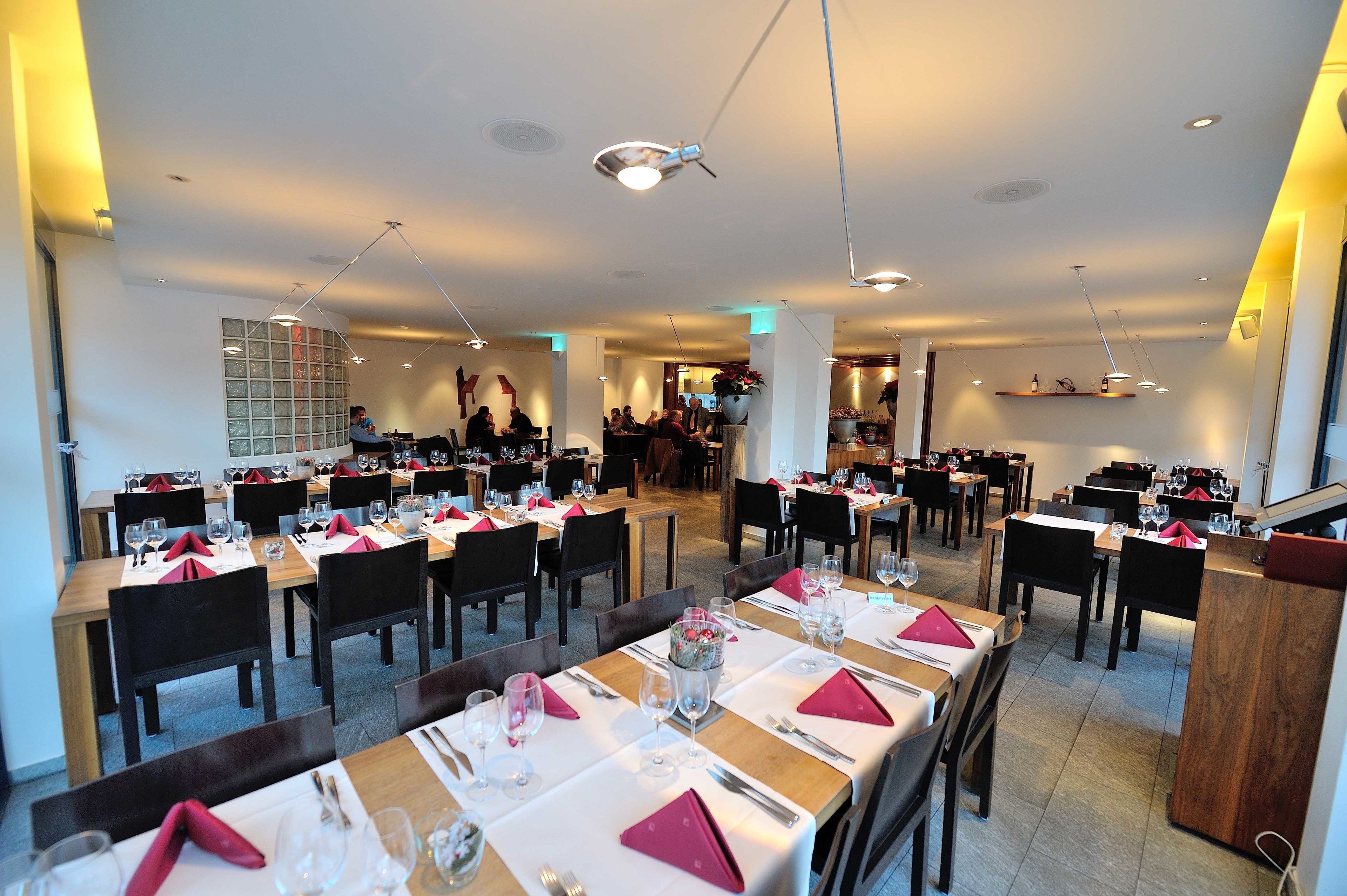 A restaurant with multiple dining tables set with red napkins, glasses, and cutlery.