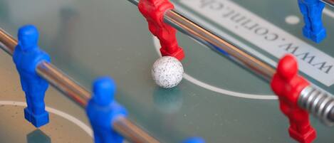 A foosball table with red and blue figures, a white ball, and a table with a logo.