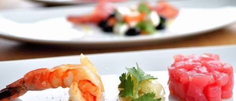 A plate with a shrimp, a small salad, and a piece of raw fish.