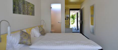 Habitación de hotel con cama, almohadas, un cuadro y vista al área de la cocina.