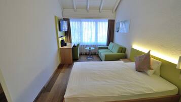 A hotel room with a bed, a green sofa, a small table, a TV, and a window with curtains.