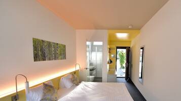 Une chambre d’hôtel moderne avec un grand lit, une table de chevet, une lampe fixée au mur et un tableau.