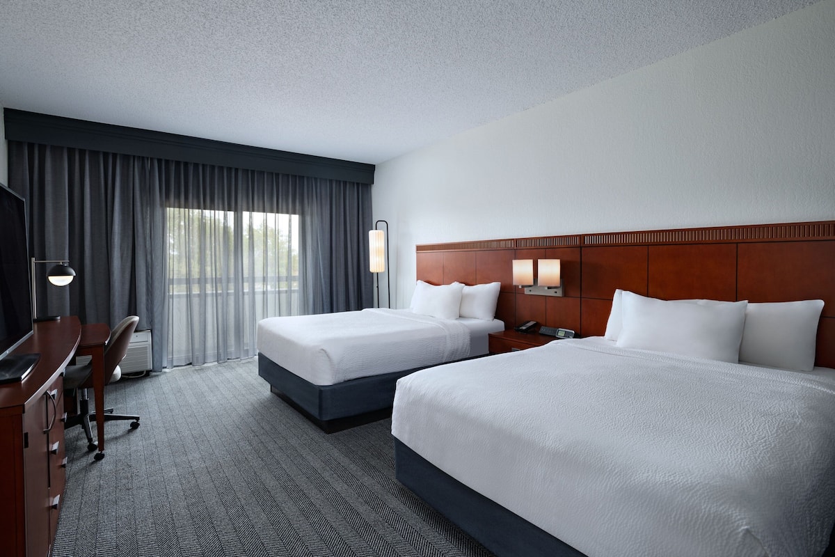 A hotel room with two beds, a desk, and a chair.