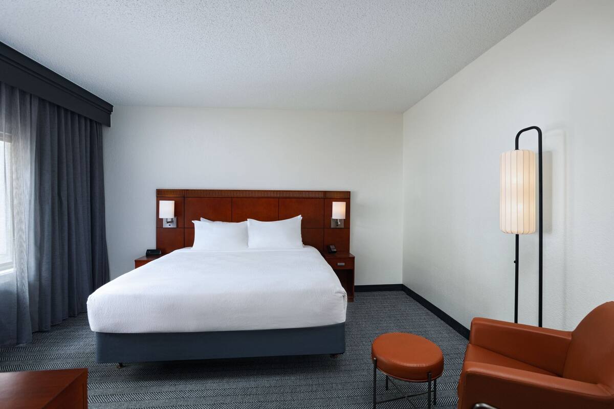 A hotel room with a large bed, a nightstand, a lamp, and a chair.
