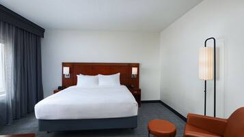 A hotel room with a large bed, a nightstand, a lamp, and a chair.