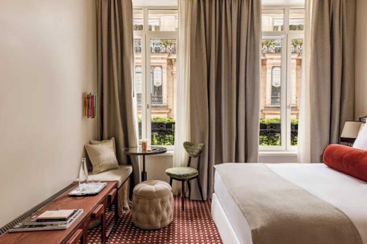 A hotel room with a bed, a small table, a chair, a sofa, and a window with curtains.