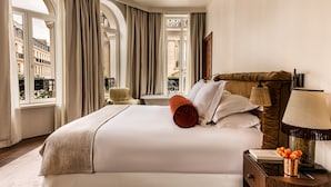 A hotel room with a large bed, a nightstand with a lamp, and a view of the city through large windows. - Chateau des Fleurs Hotel & Spa Paris (Paris)