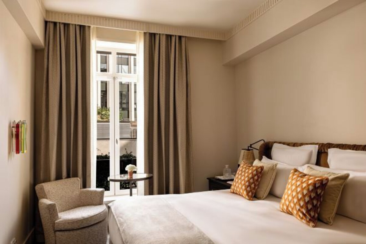 Ett hotellrum med en säng, en stol, ett litet bord och utsikt genom ett fönster.