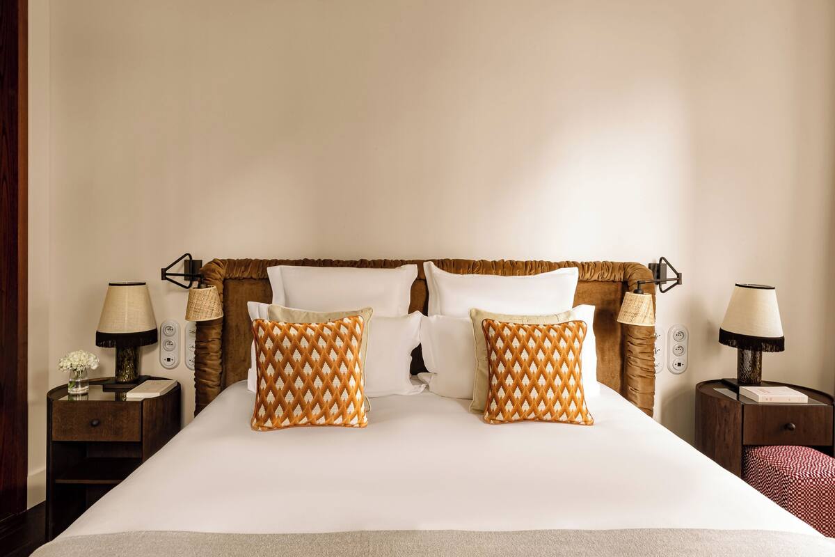 A neatly made bed with two patterned pillows, two bedside lamps, and a wooden headboard.