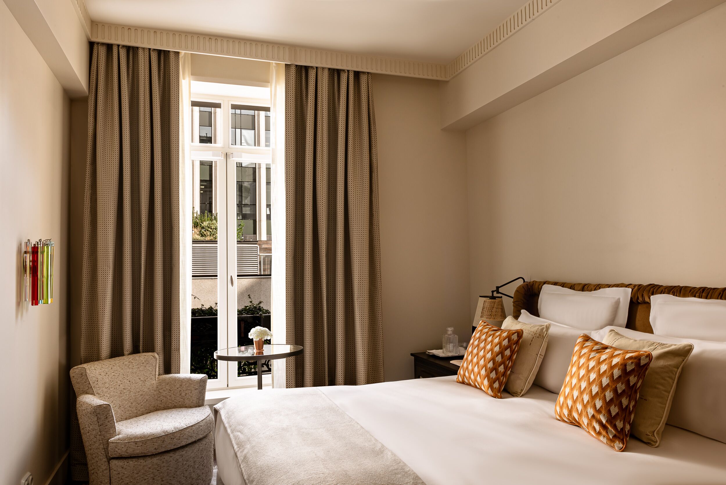 Une chambre d’hôtel avec un lit, une chaise, une petite table et des rideaux.