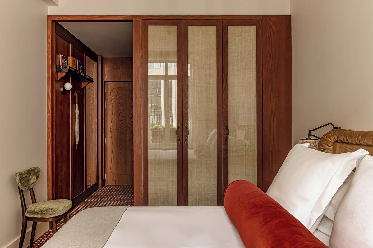 A bedroom with a large bed, a wooden wardrobe, and a chair.