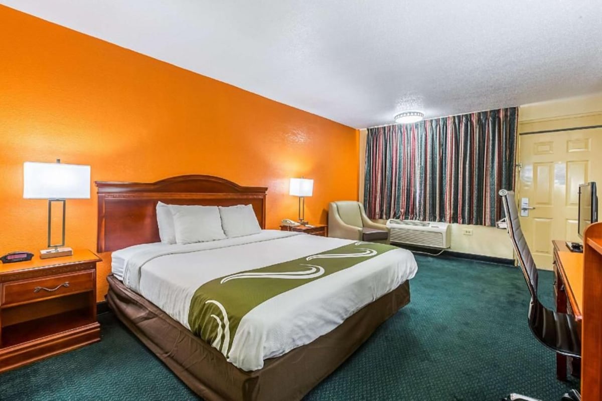 A hotel room with a large bed, a desk, a chair, a television, and a window with curtains.