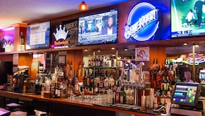 Un bar con varias pantallas mostrando contenido deportivo, una variedad de botellas de licor y una caja registradora.