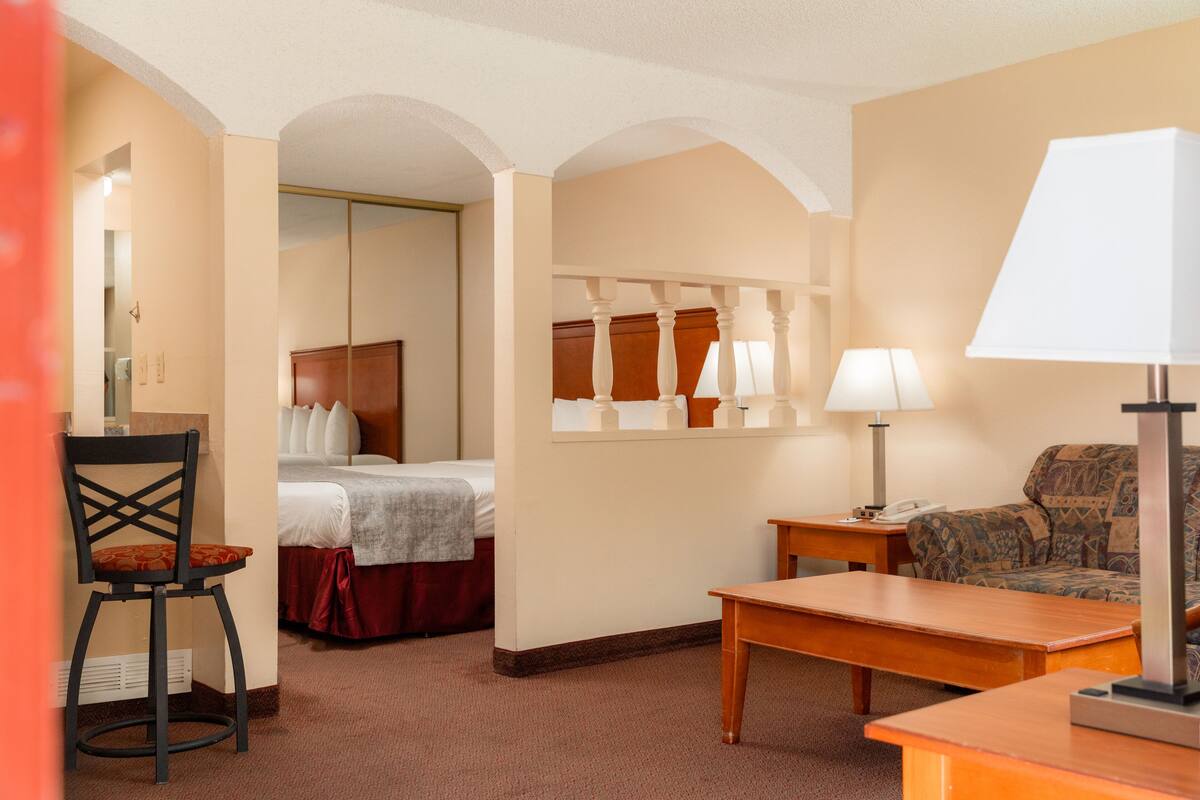 A hotel room with a bed, a desk, a chair, a sofa, and a lamp.