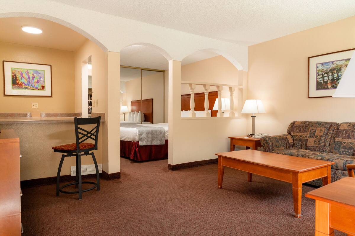 A hotel room with a bed, a sofa, a wooden table, a chair, a desk, and a lamp.