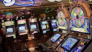 Fila de máquinas tragamonedas en un casino, con luces de neón y una ruleta.