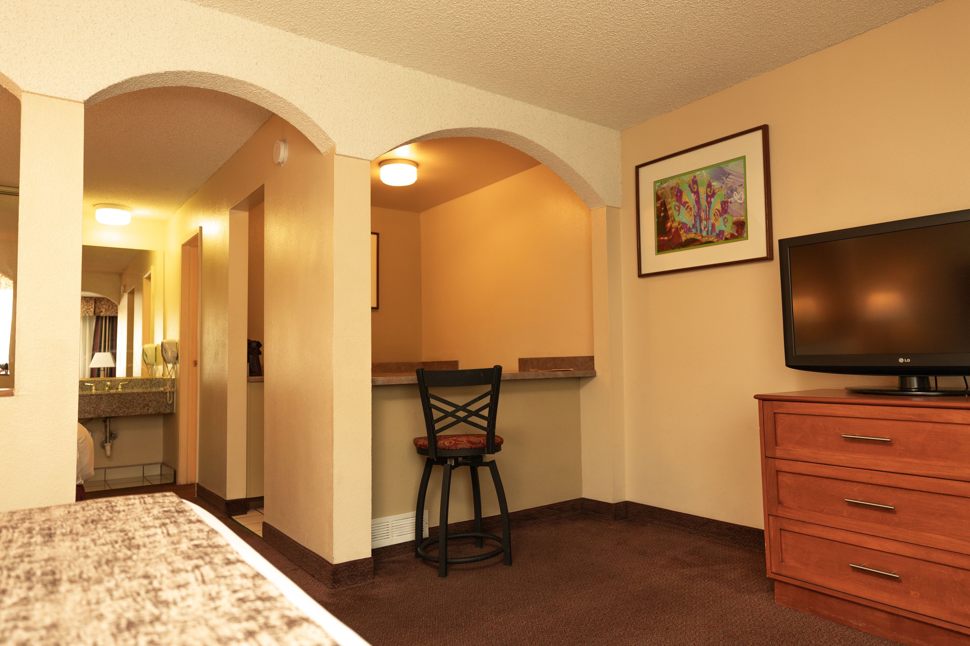 A hotel room with a bed, a desk with a chair, a television, and a dresser.