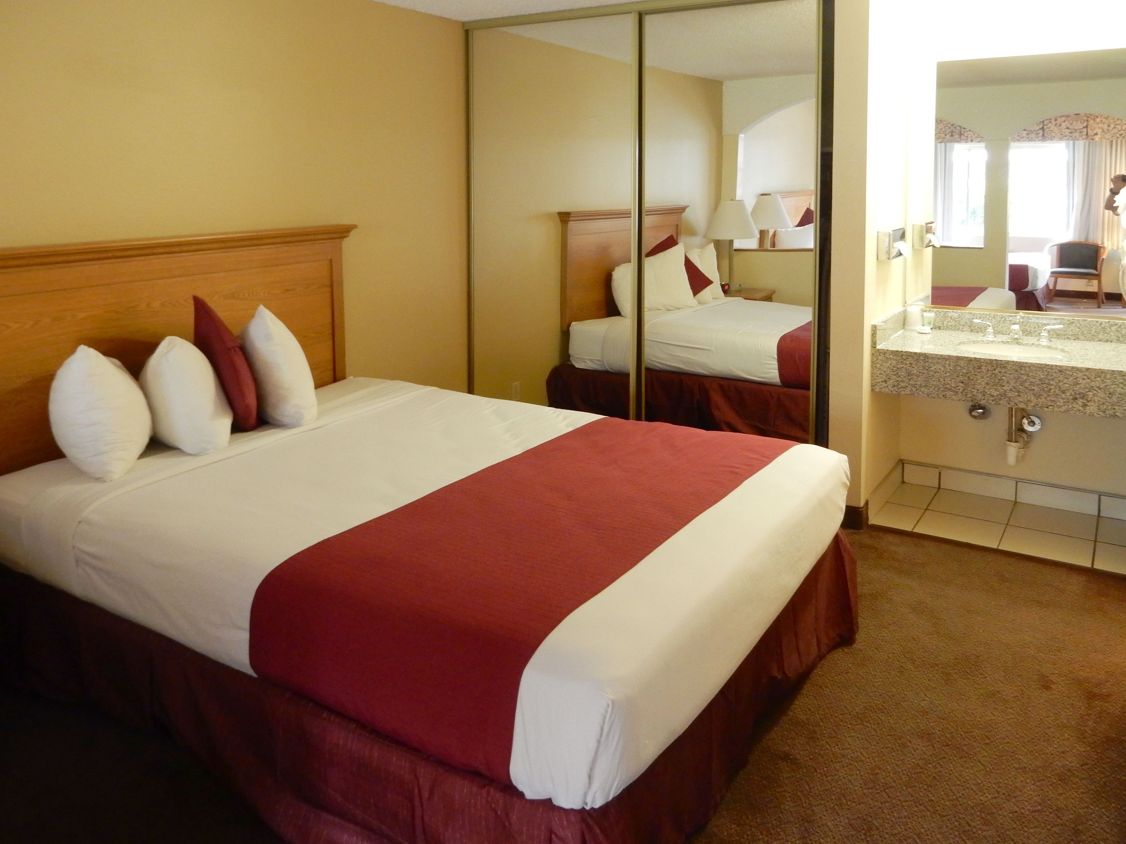 A hotel room with a bed, a mirror, and a bathroom with a sink and mirror.